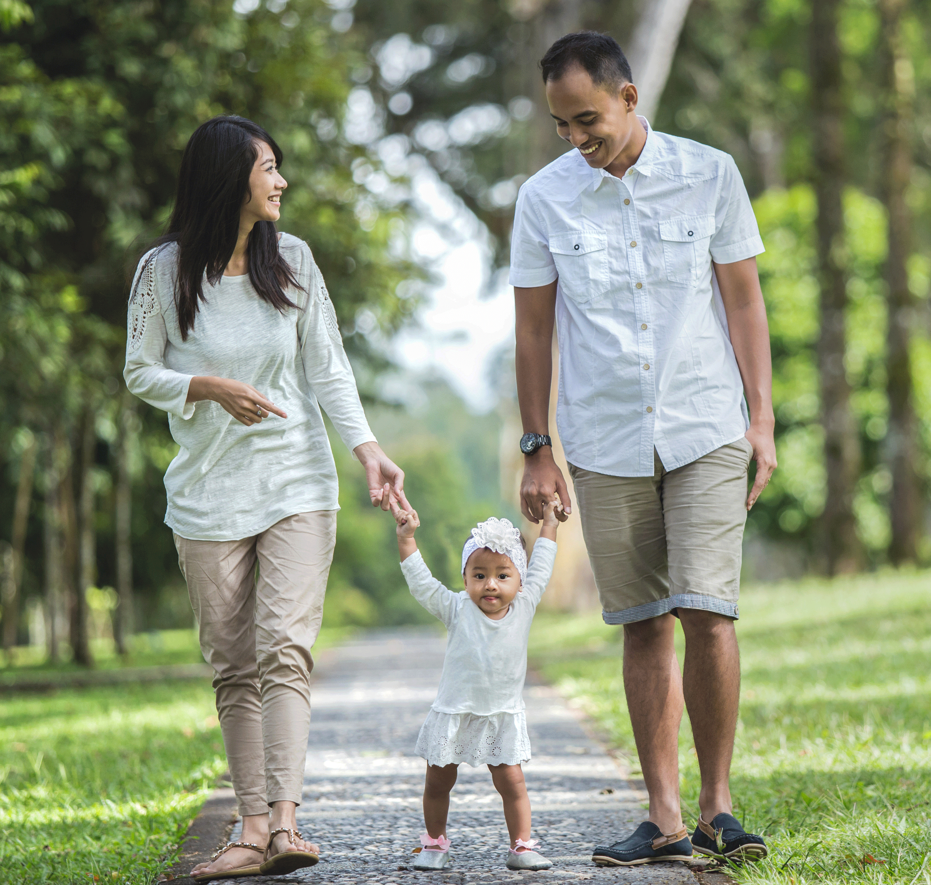 Happy young couple standing together outside on a bright sunny day, while holding their baby son.